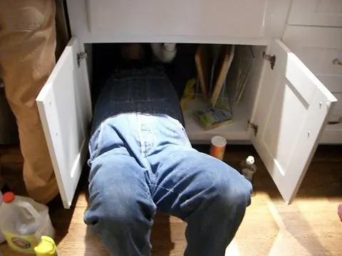 A plumber lying under a kitchen sink, fixing the pipes